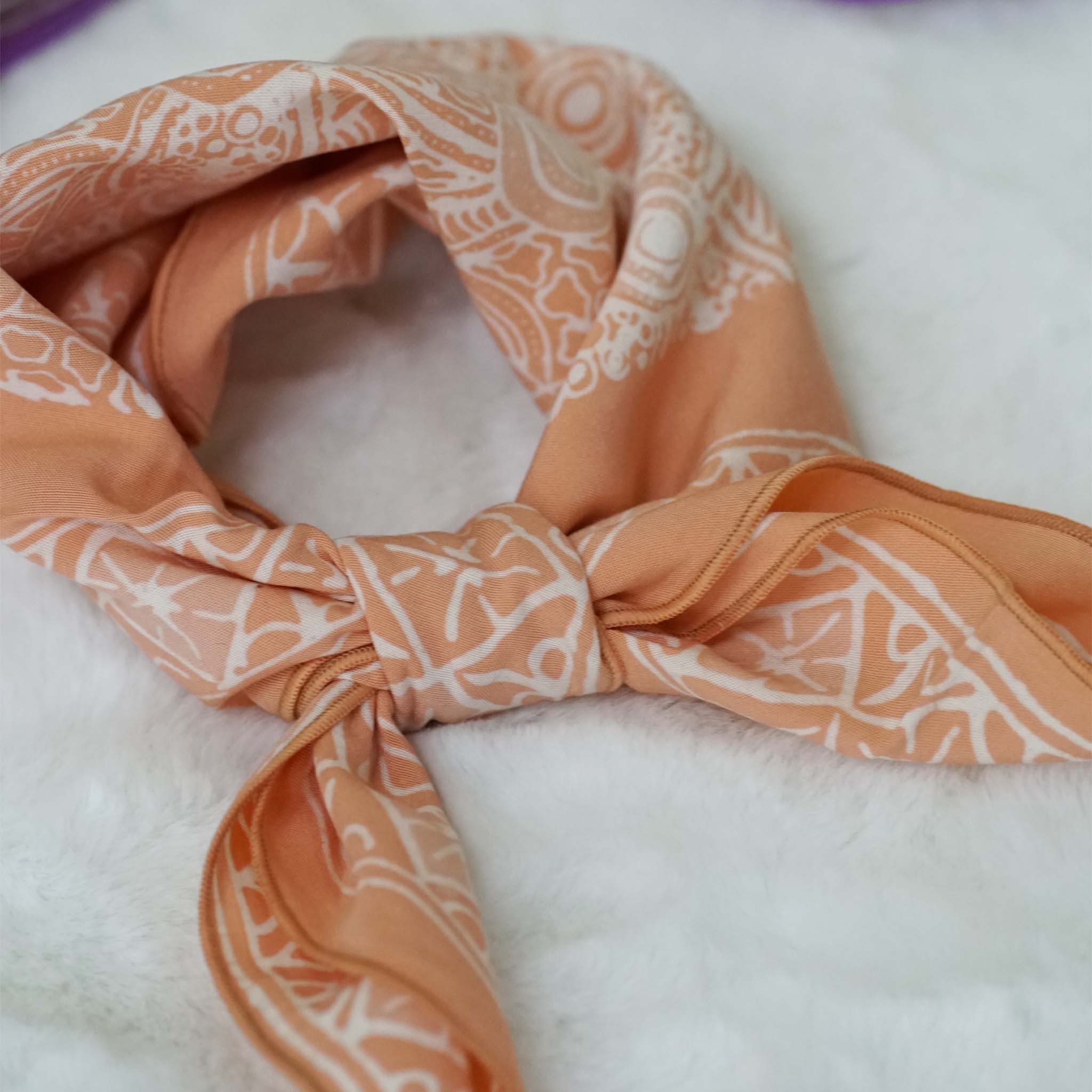 A peach-colored cotton bandana with a hand-dyed batik pattern laid out on a white surface.