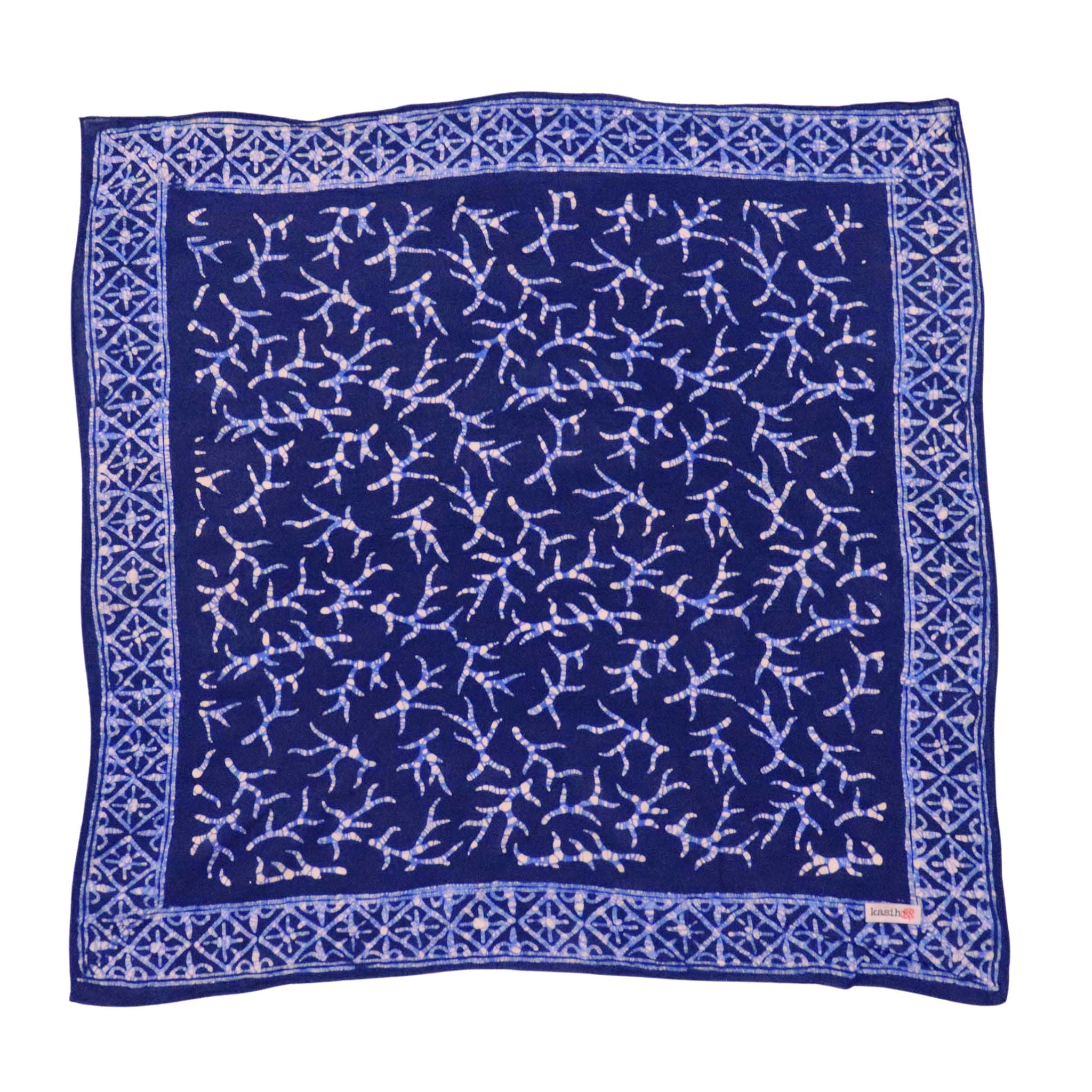 A navy blue bandana with a hand-stamped batik pattern in white, displayed flat.