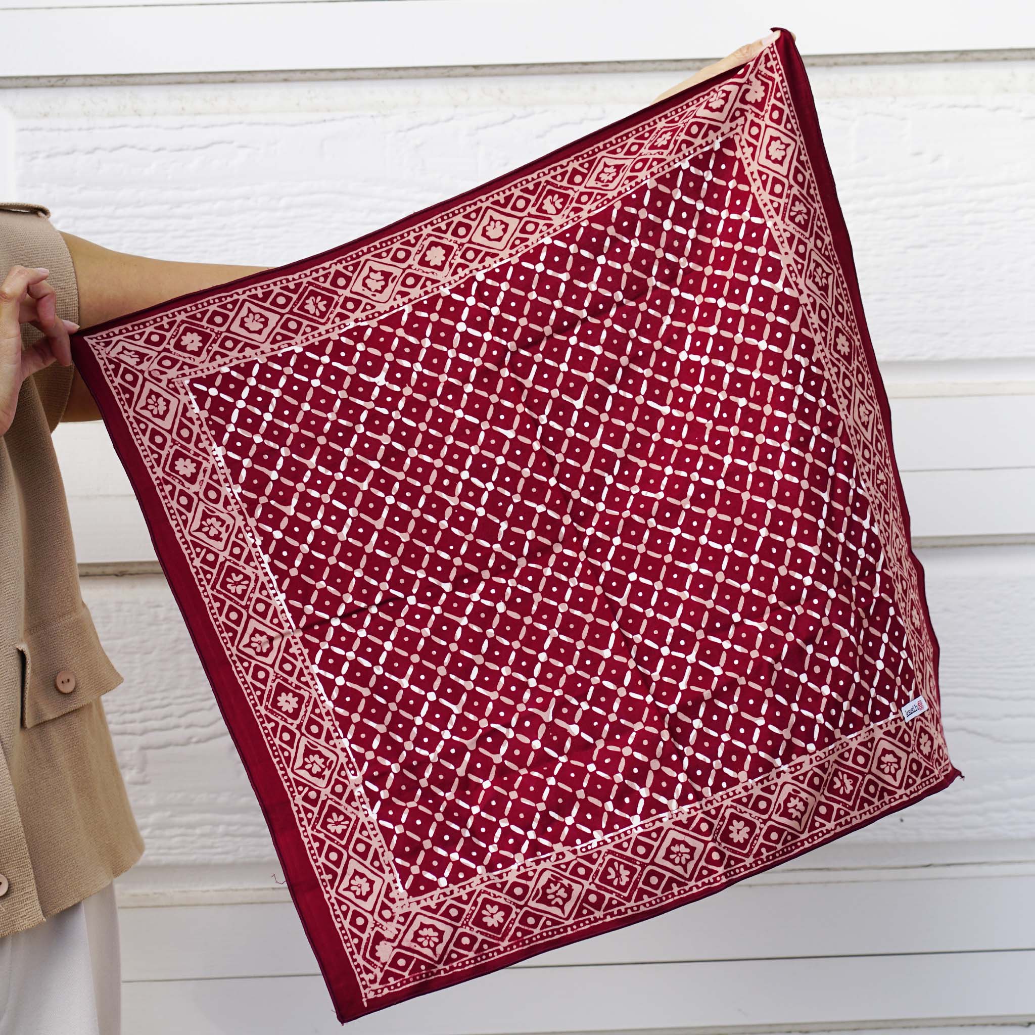 A person holding a red and white geometric patterned cotton batik bandana.