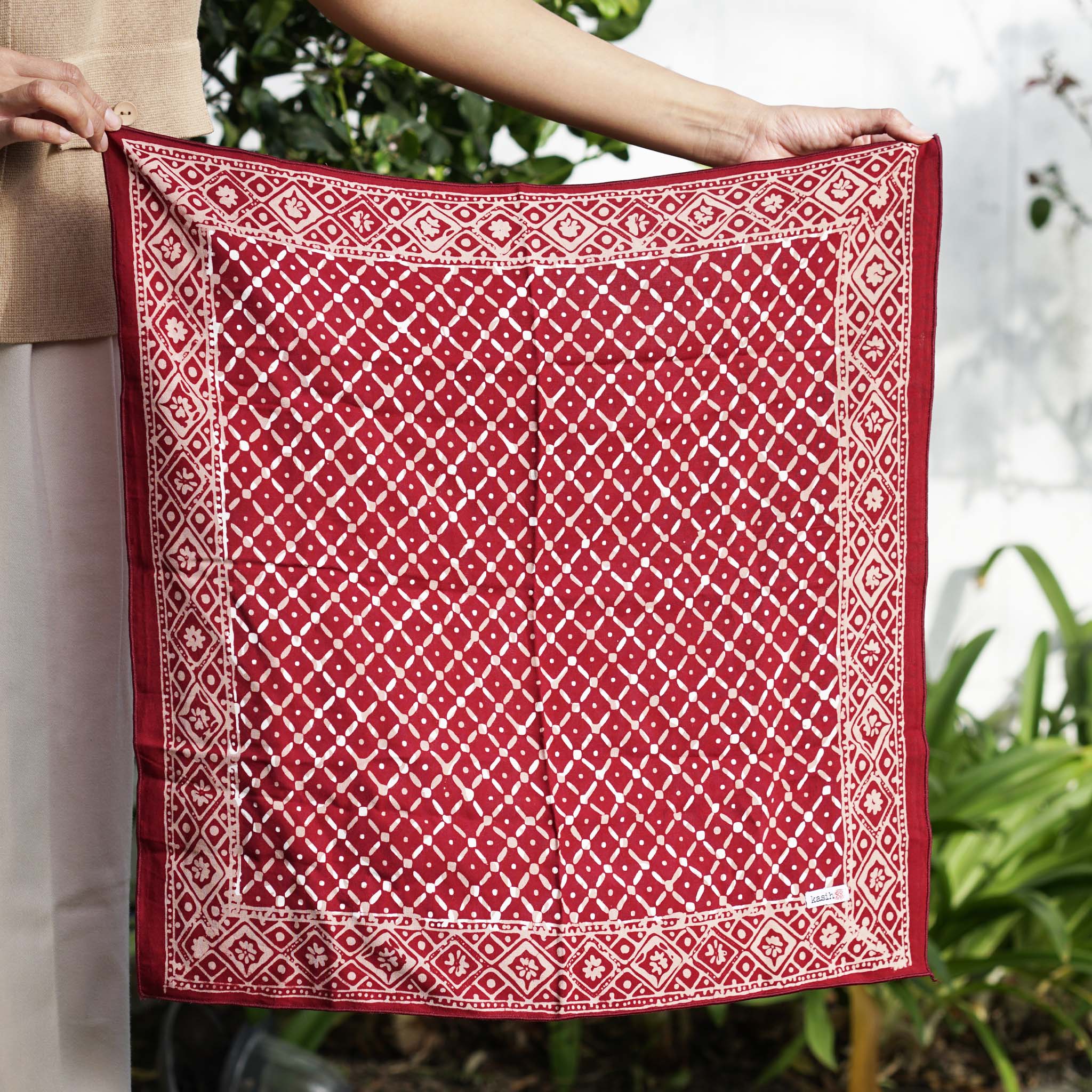 A person holding a red and white geometric patterned cotton batik bandana.