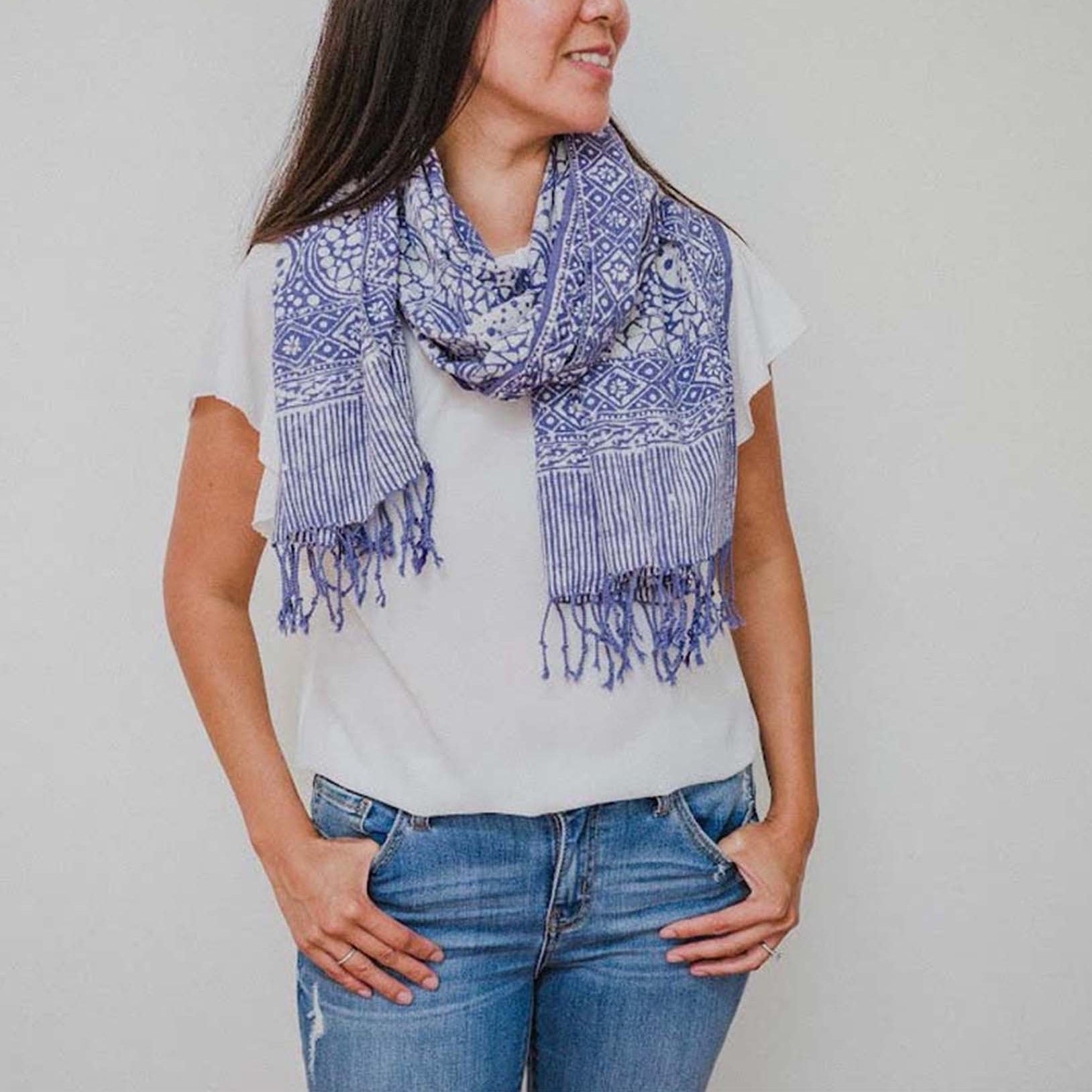 Woman wearing a blue patterned scarf and jeans against a plain background