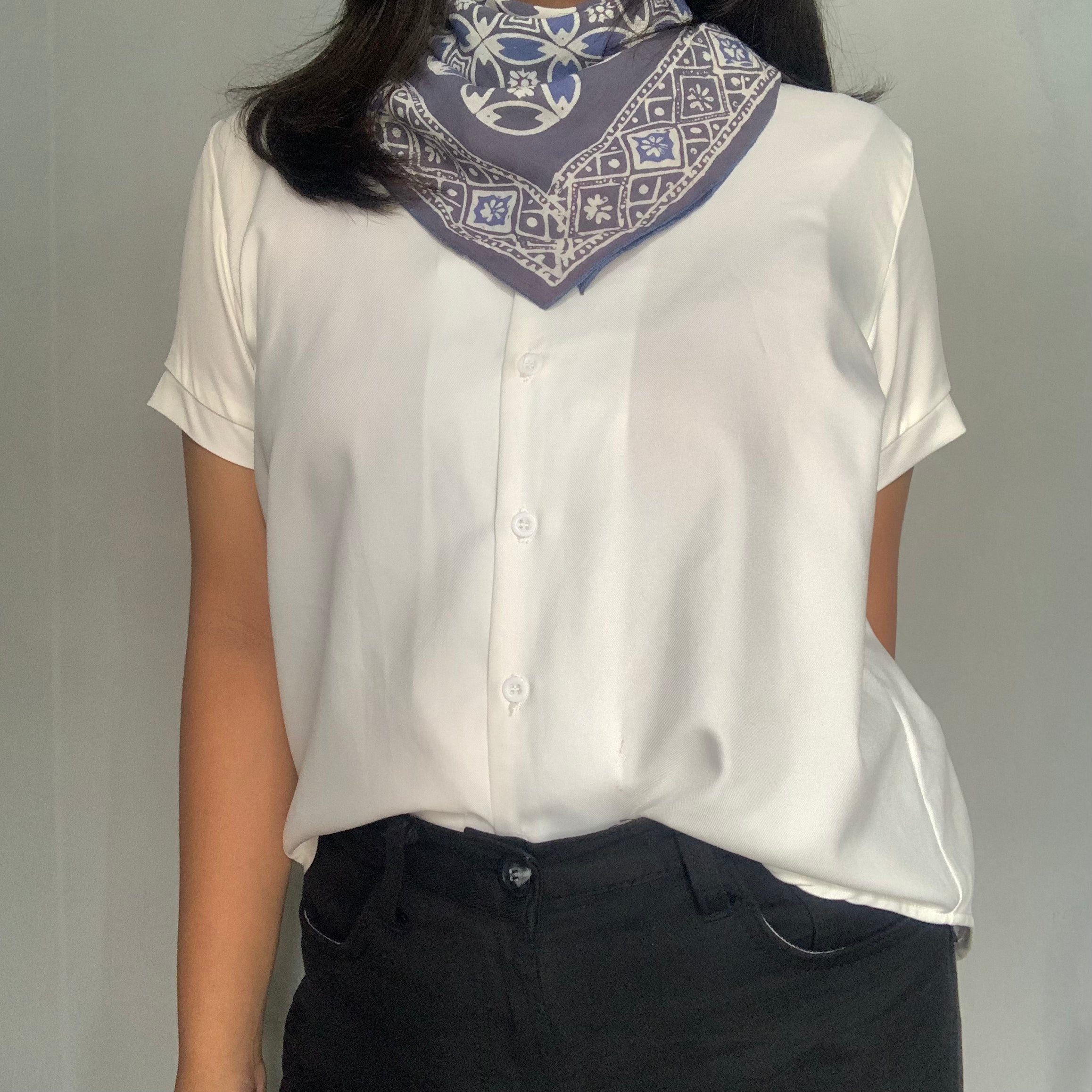 Person wearing a white blouse with a patterned scarf on a plain background