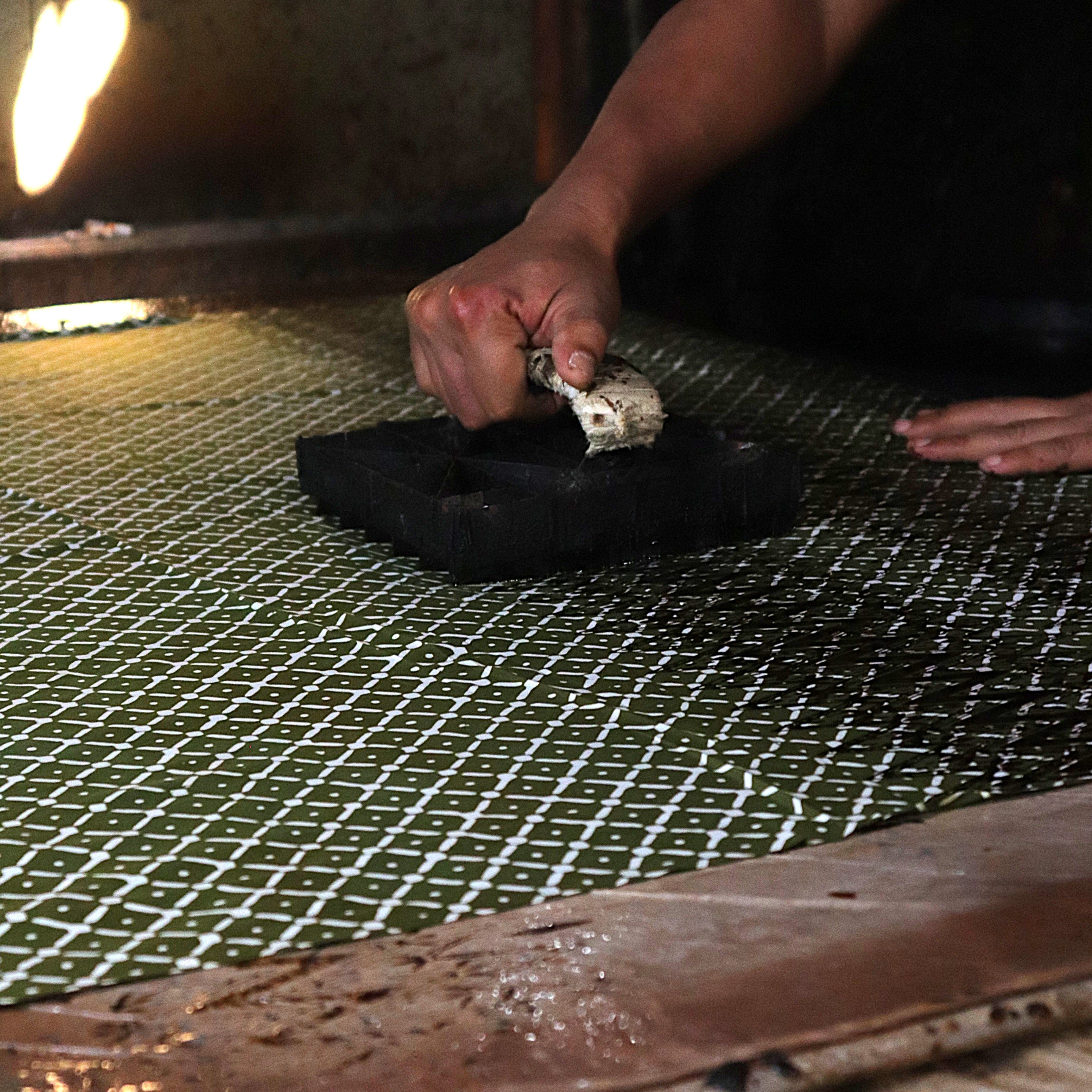 Person holding a batik copper stamp over a 100% cotton fabric surface with a flame in the background