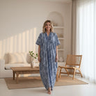 Woman wearing a blue patterned dress standing in a bright living room.